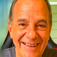 Close-up of a smiling older man in a gray t-shirt.