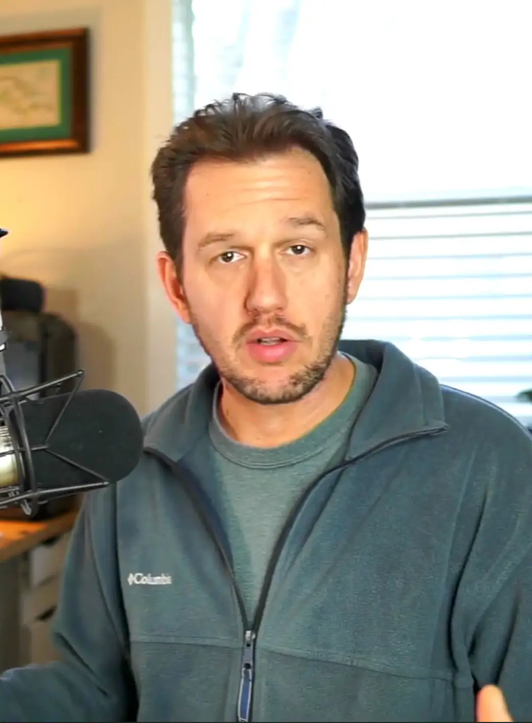 Man in a blue fleece jacket speaking into a microphone.