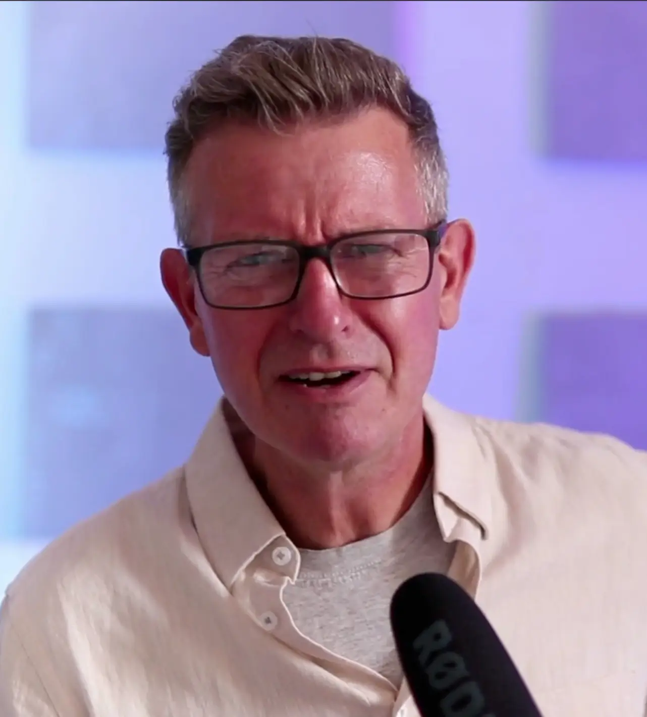 Man with glasses speaking into a microphone in a studio.