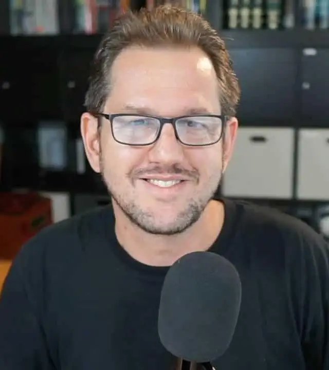 Smiling man with glasses and a microphone.